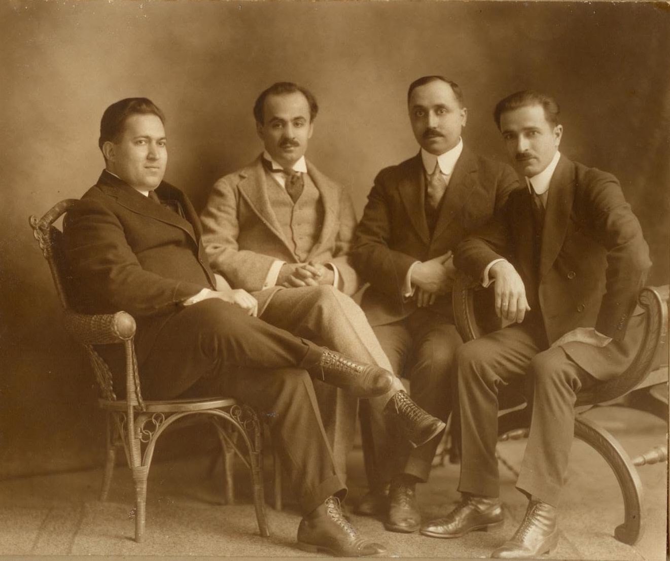 Sepia group photograph of four men in suits seated together: Naseeb Arida, Kahlil Gibran, Abdulmassih Haddad and Mikhail Naimy